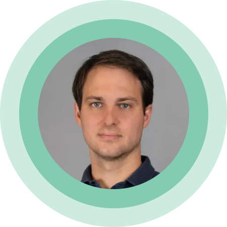 A headshot of a man with a neutral expression and a mint green circular border around the image.