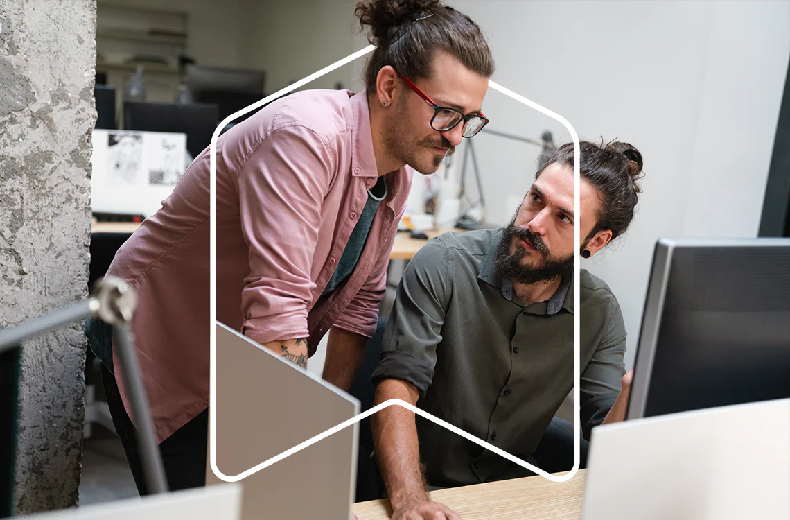 Two men working together at a desk in an office using computers