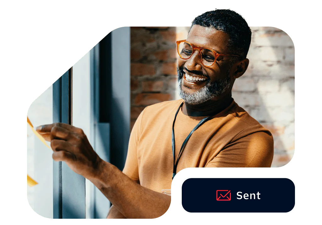 Man with glasses smiling and pointing at something near a window