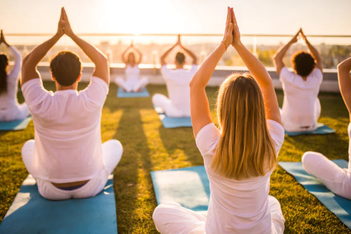 Back view of group of relaxed people exercising Yoga with their arms raised on a terrace. Back view of group of relaxed people exercising Yoga with their arms raised on a terrace.