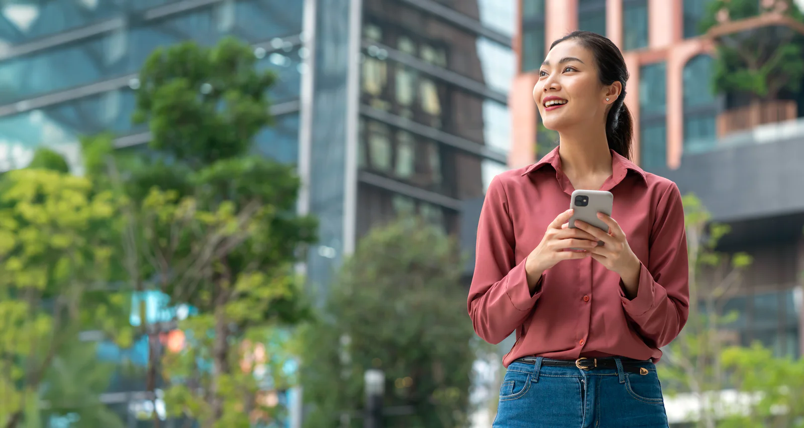 Young caucasian man holding mobile on the street in the city. Happy male wearing headphones and using cell outdoors, looking and checking his social media. Vertical image with copy space.