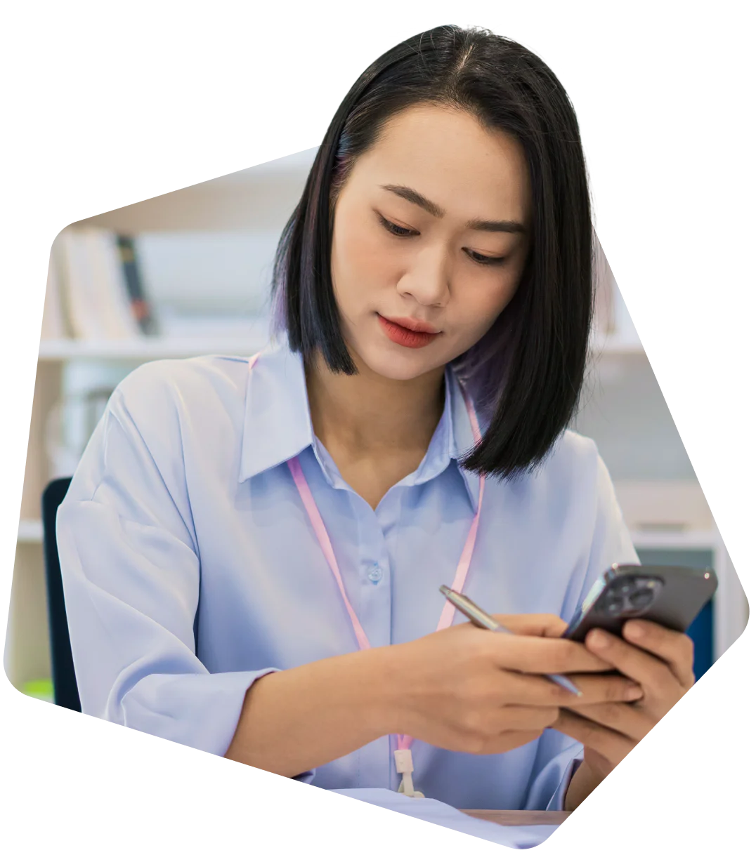 Woman in a light purple shirt holds her phone and makes a fist as she looks at the screen with a smile.