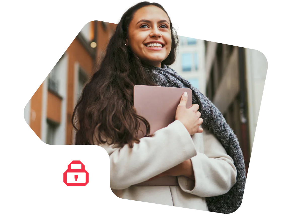 Smiling woman holding a pink tablet while wearing a grey scarf and coat in an urban setting.