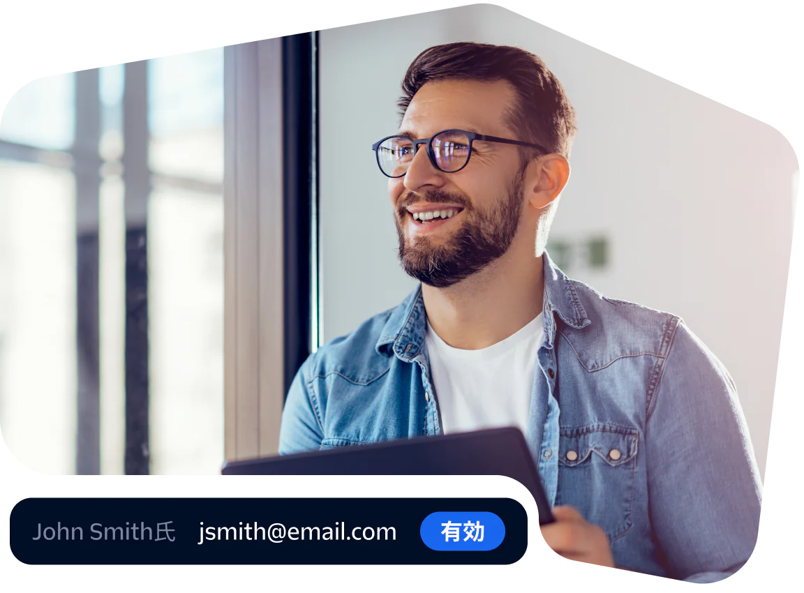Smiling professional verifying email with a tablet Man in glasses and denim shirt smiling while using a tablet near a window.