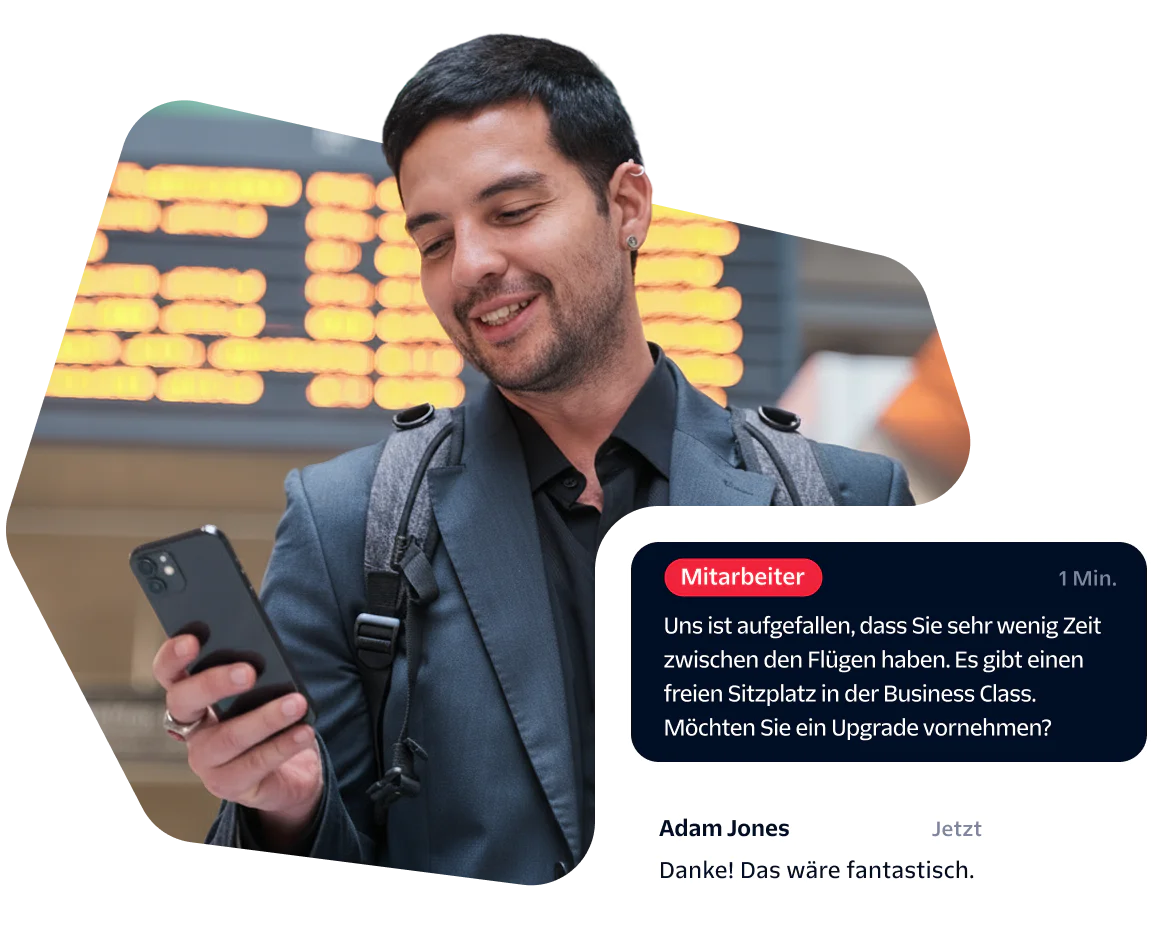 Man checks phone at airport, receives message about upgrading to business class, smiles.