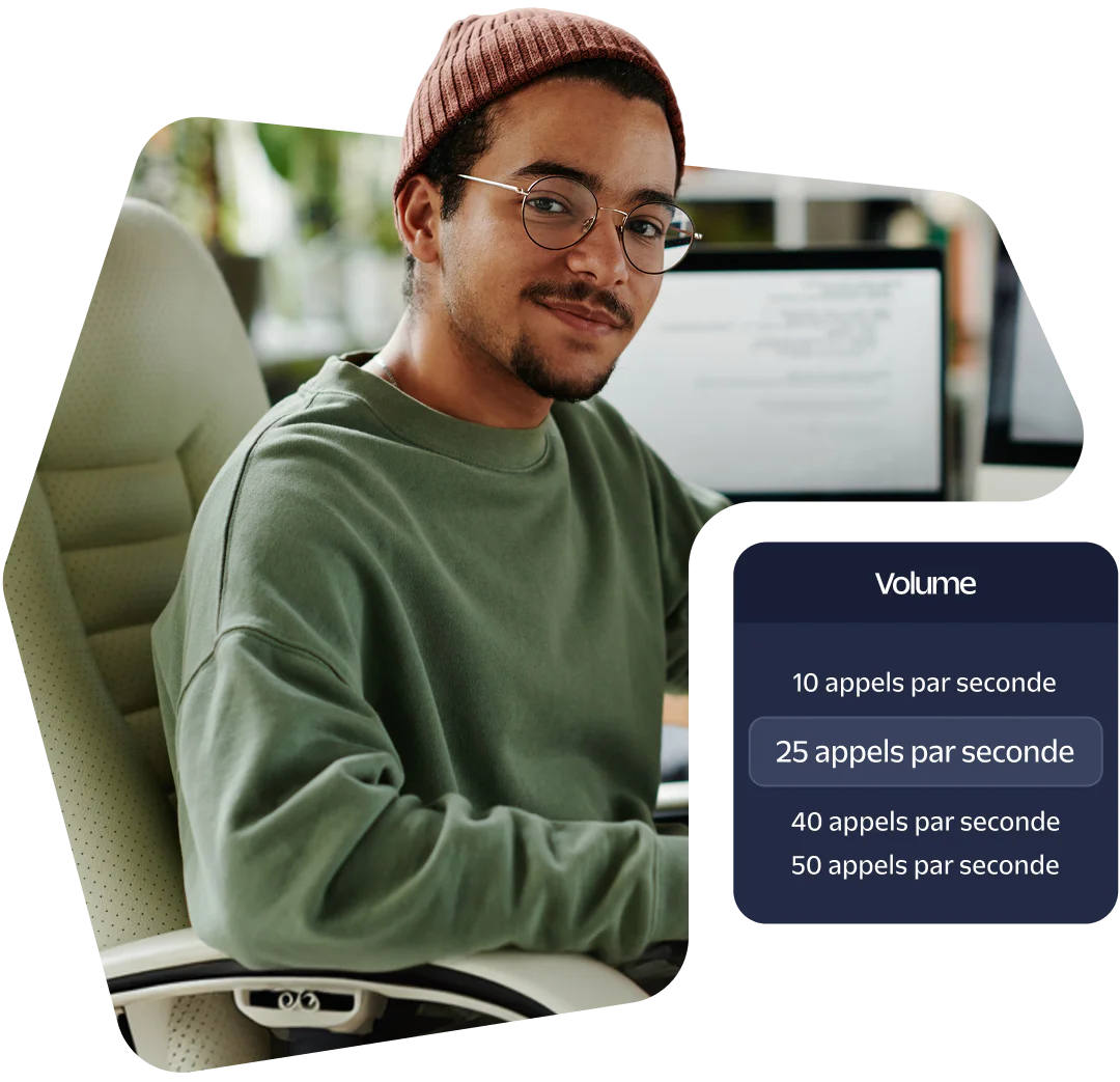 A person wearing glasses and a beanie sitting at a desk with a computer screen showing call volume data.