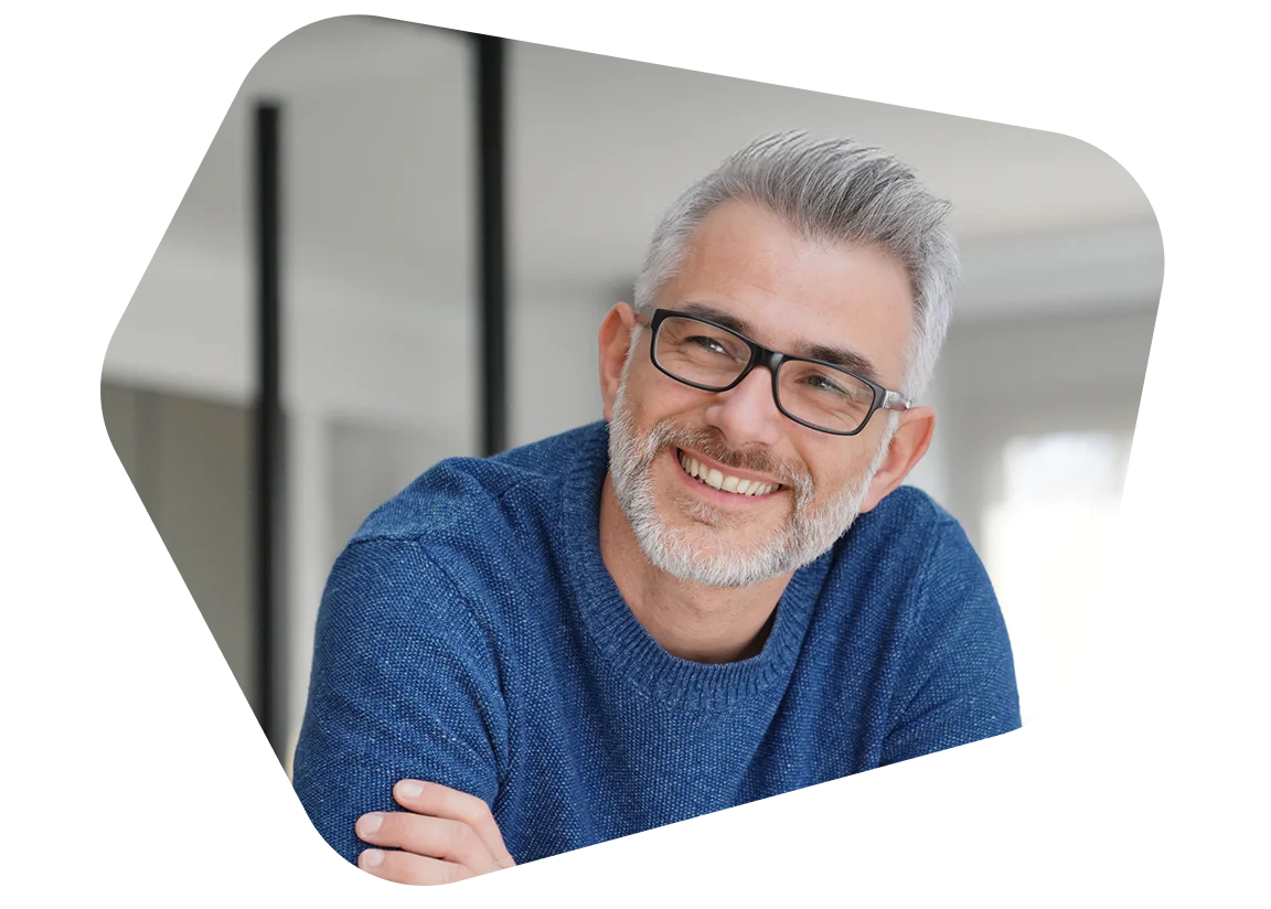 Smiling man with glasses in blue sweater indoors Man with grey hair and glasses wearing a blue sweater smiling indoors