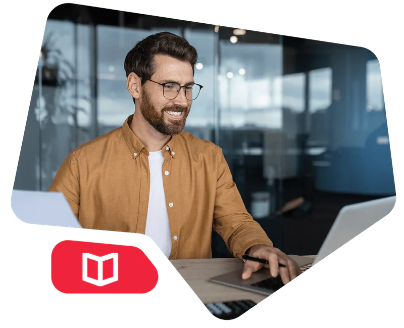 Man in a brown shirt and glasses using a laptop at an office desk.