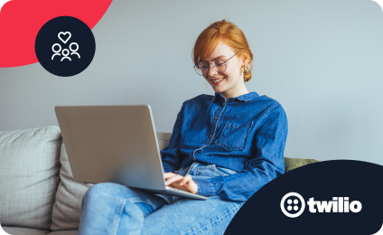 Woman wearing denim, smiling, working on a laptop while seated on a couch.