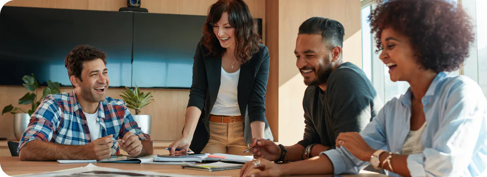 Four colleagues laughing and collaborating during a team meeting in a modern office setting.