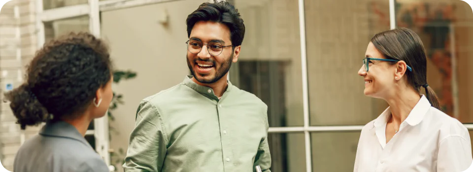 Three colleagues smiling and chatting outside a modern office building.