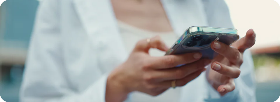 Close-up of hands holding a smartphone while typing in a casual outdoor setting.