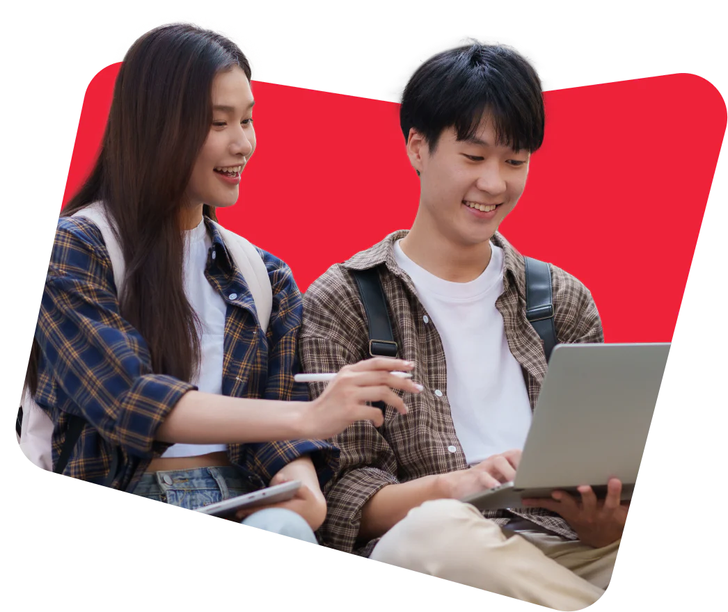 Two students with backpacks smile while working on a laptop together.