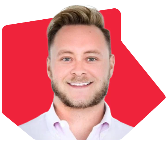Man with short blond hair and beard wearing a white collared shirt, smiling against a red background.