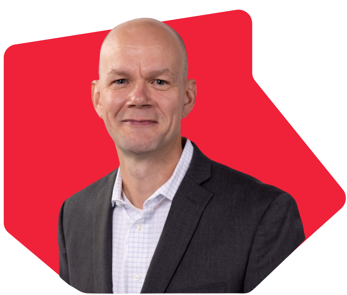 A bald man in a gray suit and white shirt with a red background behind him.
