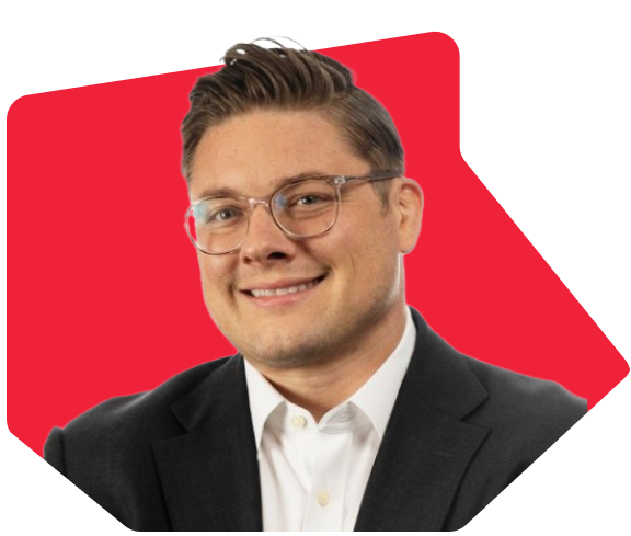 Man with glasses wearing a white shirt and dark blazer with a red background.