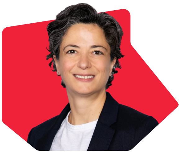 Smiling person with short hair in a blazer and white shirt with a red background.