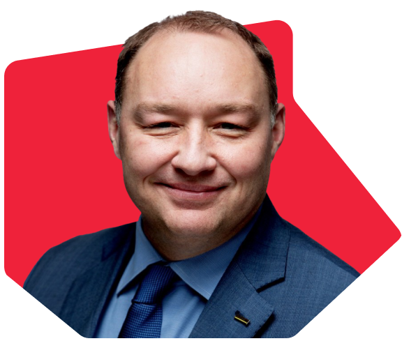 Man in a blue suit and tie smiling with a red geometric background.