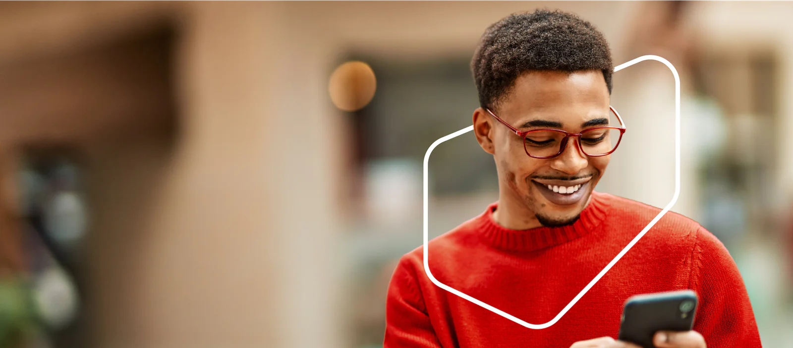 A person in a red sweater and glasses smiles while looking at their phone.