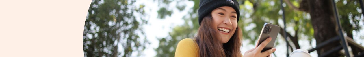 Smiling woman in a beanie looking at her smartphone with trees in the background.