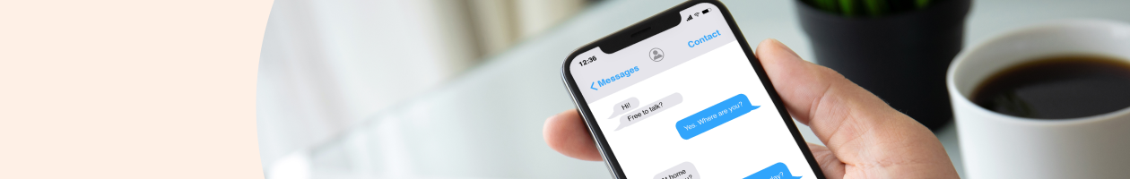 Hand holding a smartphone showing a text conversation next to a cup of coffee.