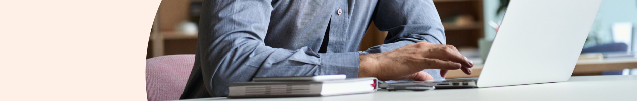 Man typing on a laptop at his desk with notebooks nearby.