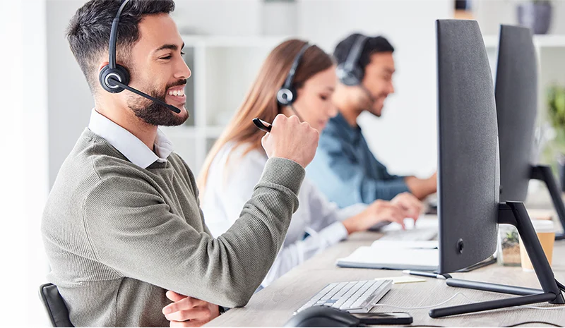 Three customer service representatives wearing headsets working at computers in an office.