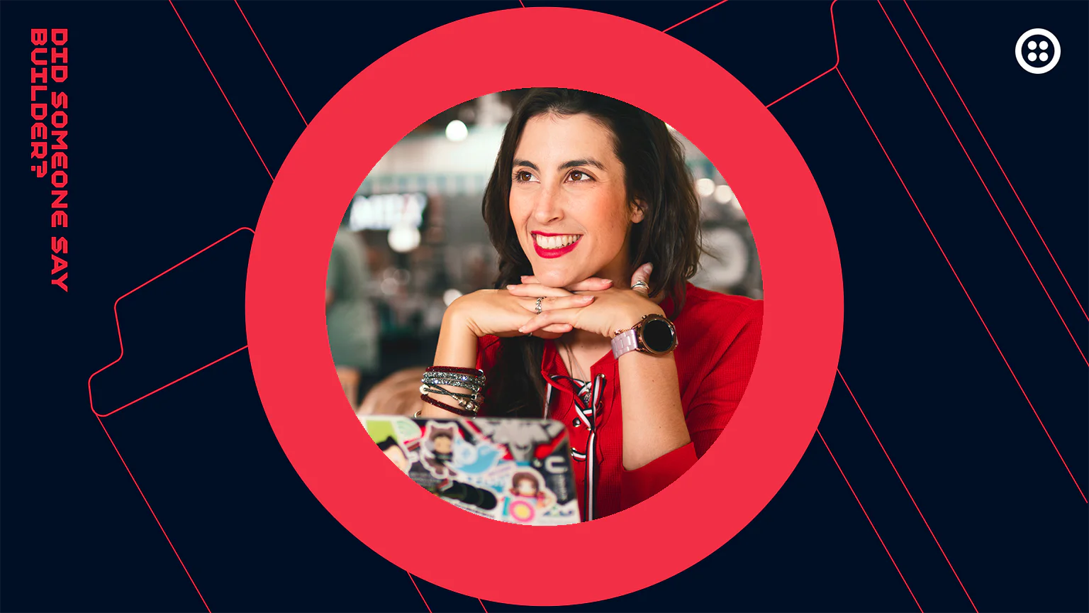 Woman in a red shirt smiling and resting her chin on her hands in a tech-themed setting.