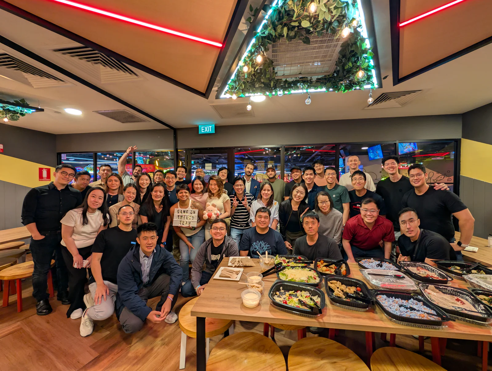 Large group of people posing for a photo in a restaurant with food on the table in front of them.