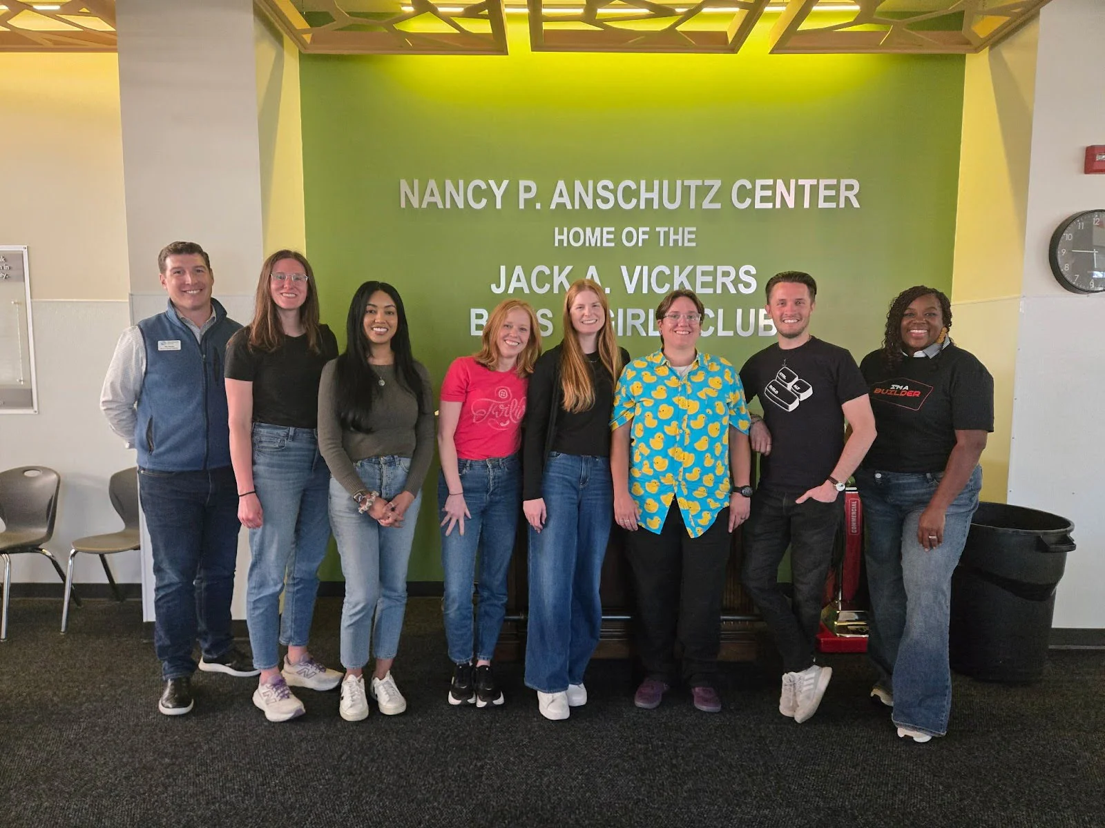 Eight individuals standing in front of green wall with Nancy P. Anschutz Center sign