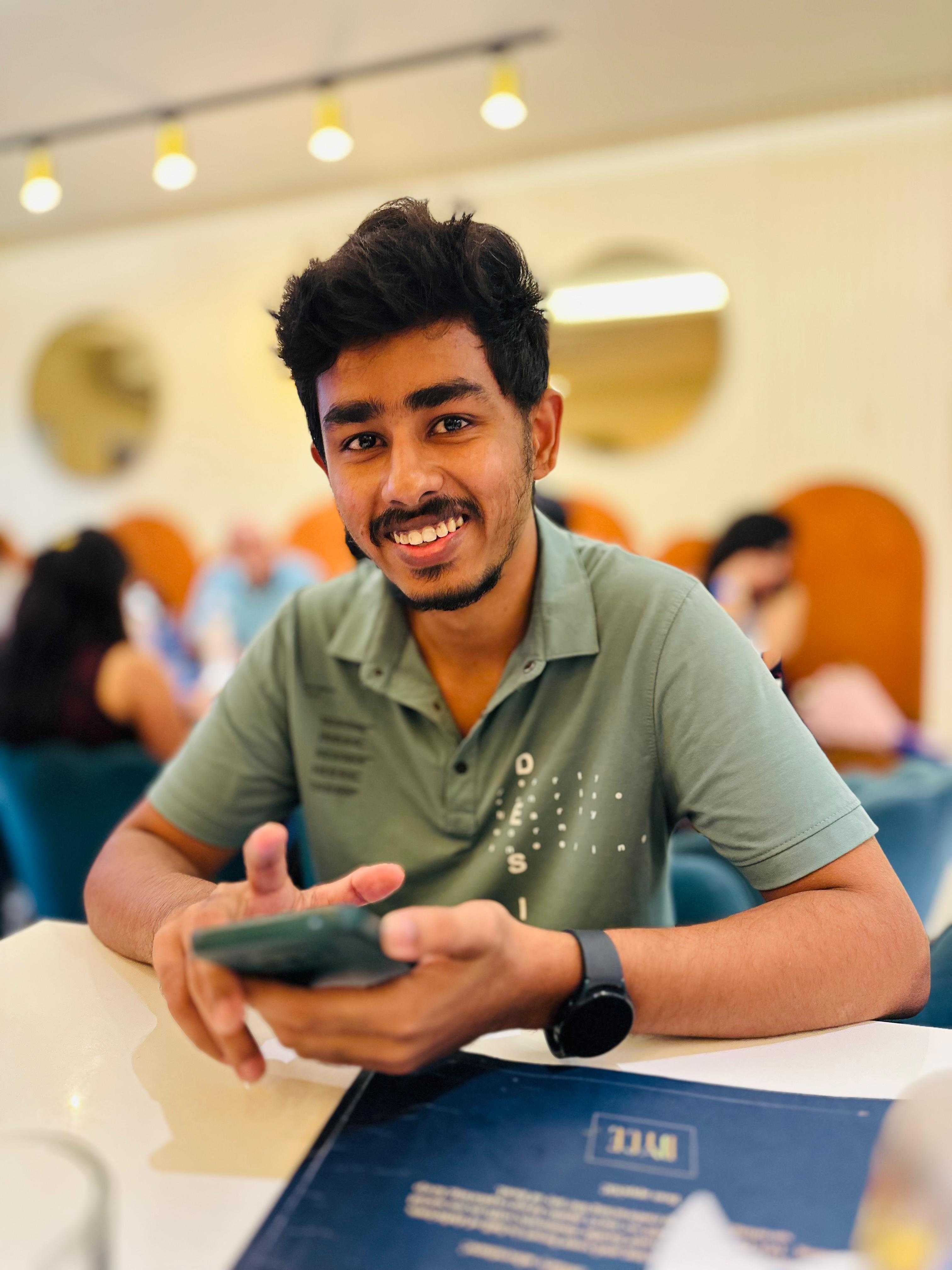 Man smiling, holding a phone and sitting at a café table