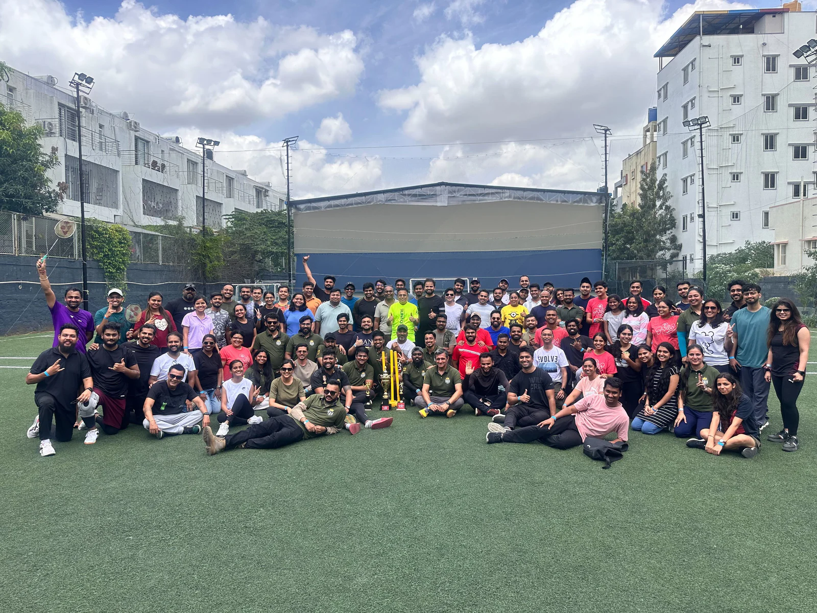 Group Picture of a Corporate Cricket Event A large group of people gathered around a cricket pitch, some holding a trophy.