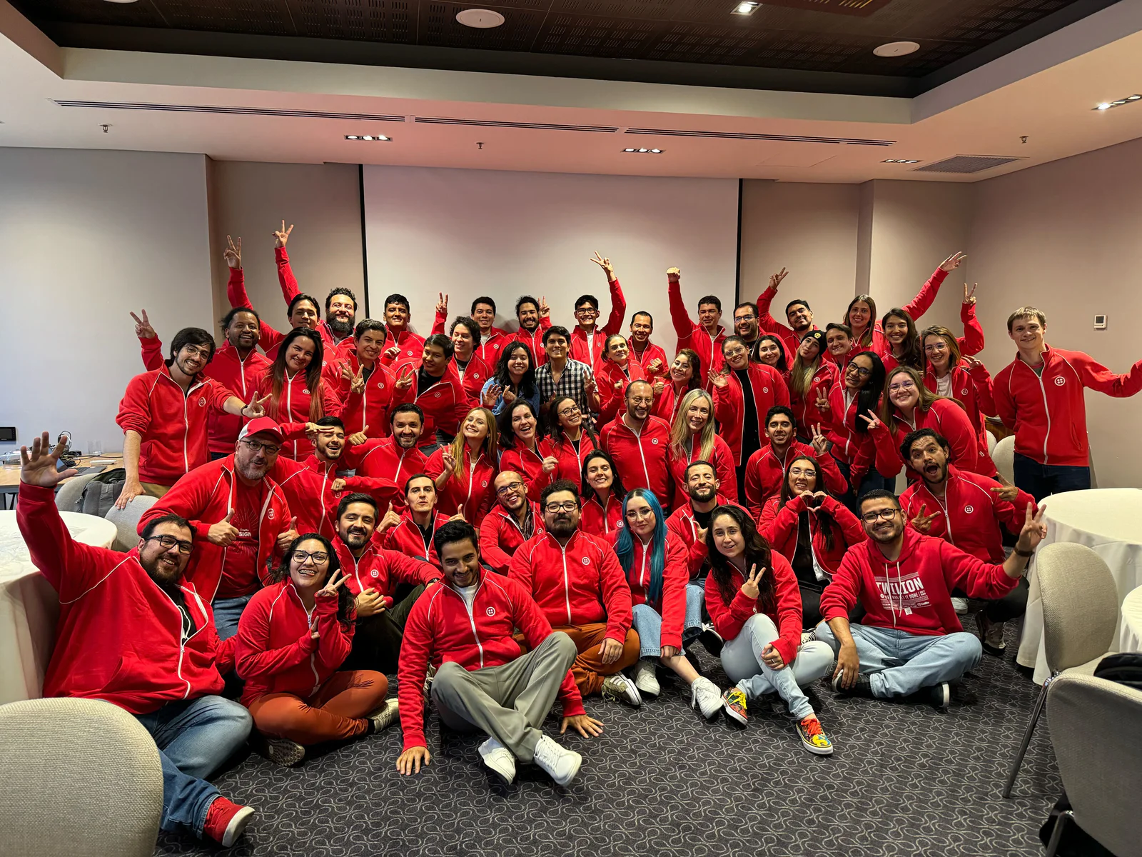 Group of People in Red Hoodies Celebrating at an Indoor Event A large group of people wearing matching red hoodies posing together in a conference room.