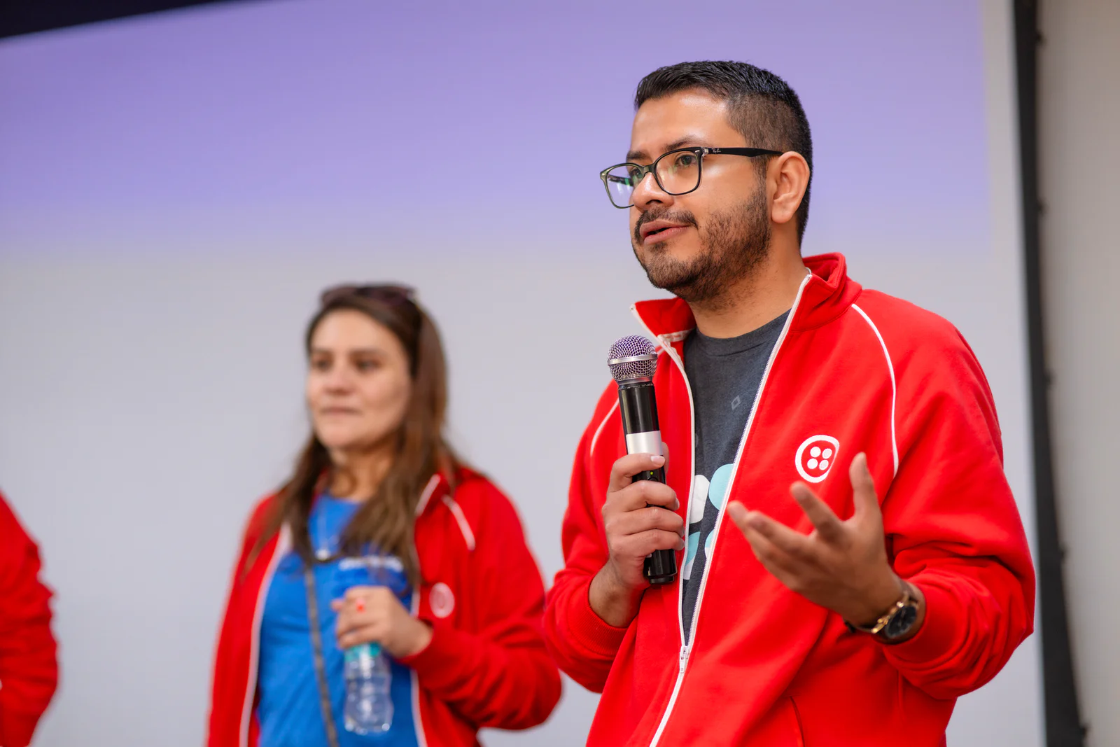 Speaker addressing an audience during a presentation Two people in red jackets with microphones speaking at an event.