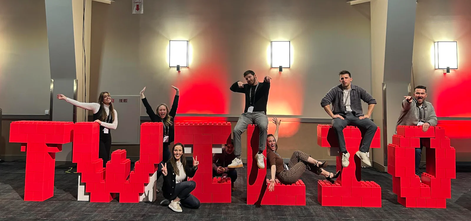 Eight people posing on and around a large red TWIST sign in a lit indoor space.