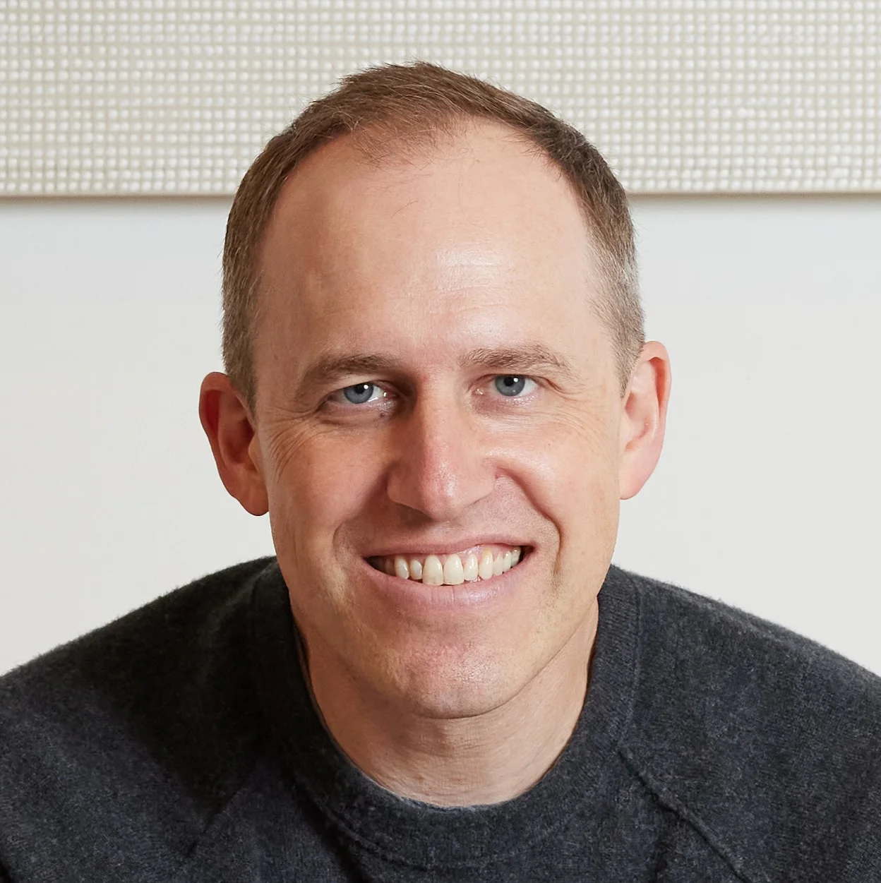 Man with short hair and a gray sweater smiling at the camera