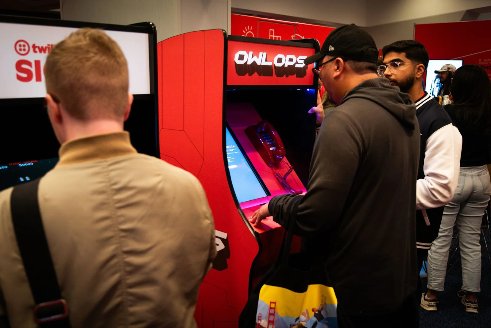 Several people standing and playing arcade games at a gaming event. Several people standing and playing arcade games at a gaming event.