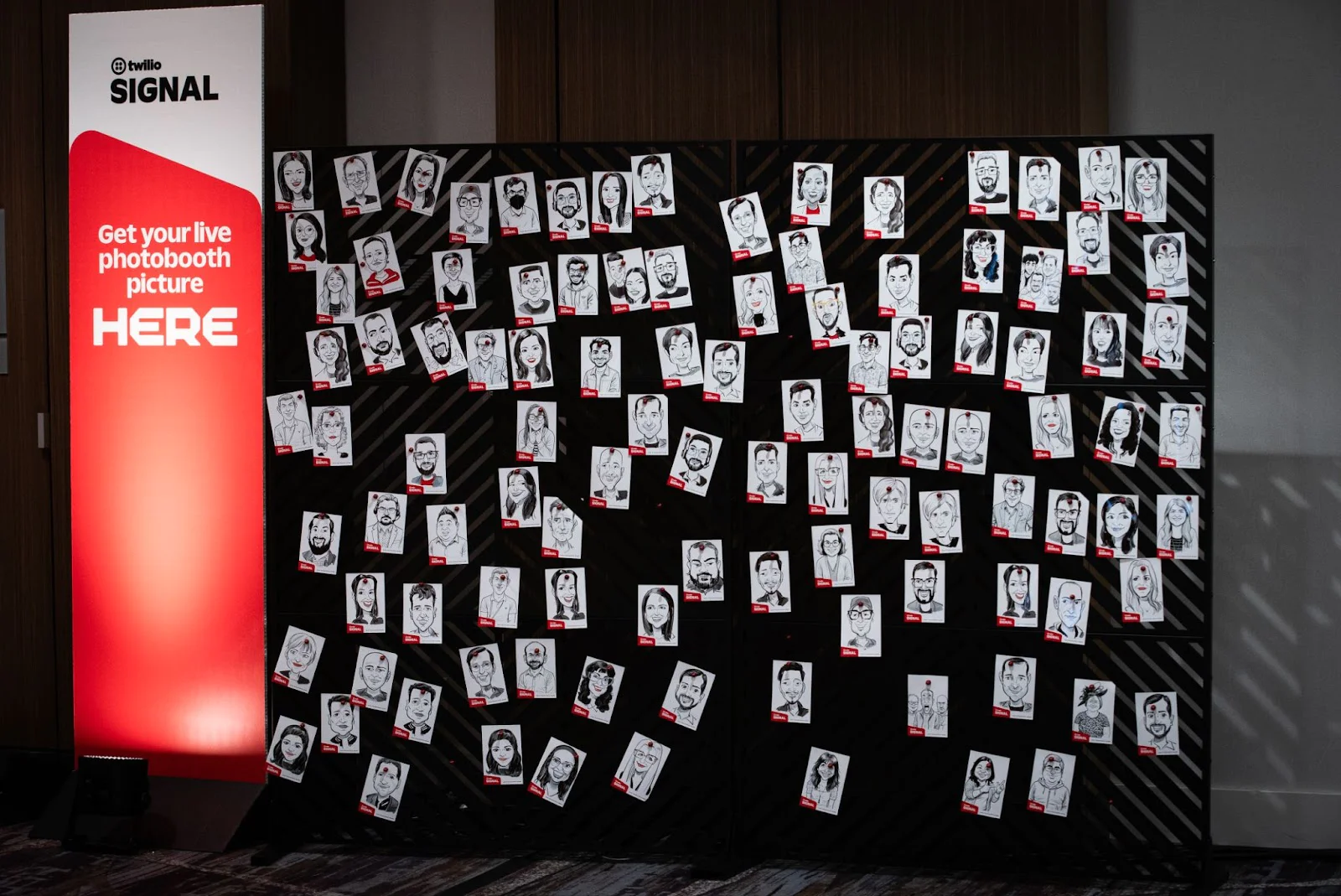 Numerous drawn portraits displayed on a board next to a red banner reading Get your live photobooth picture HERE. Numerous drawn portraits displayed on a board next to a red banner reading Get your live photobooth picture HERE.
