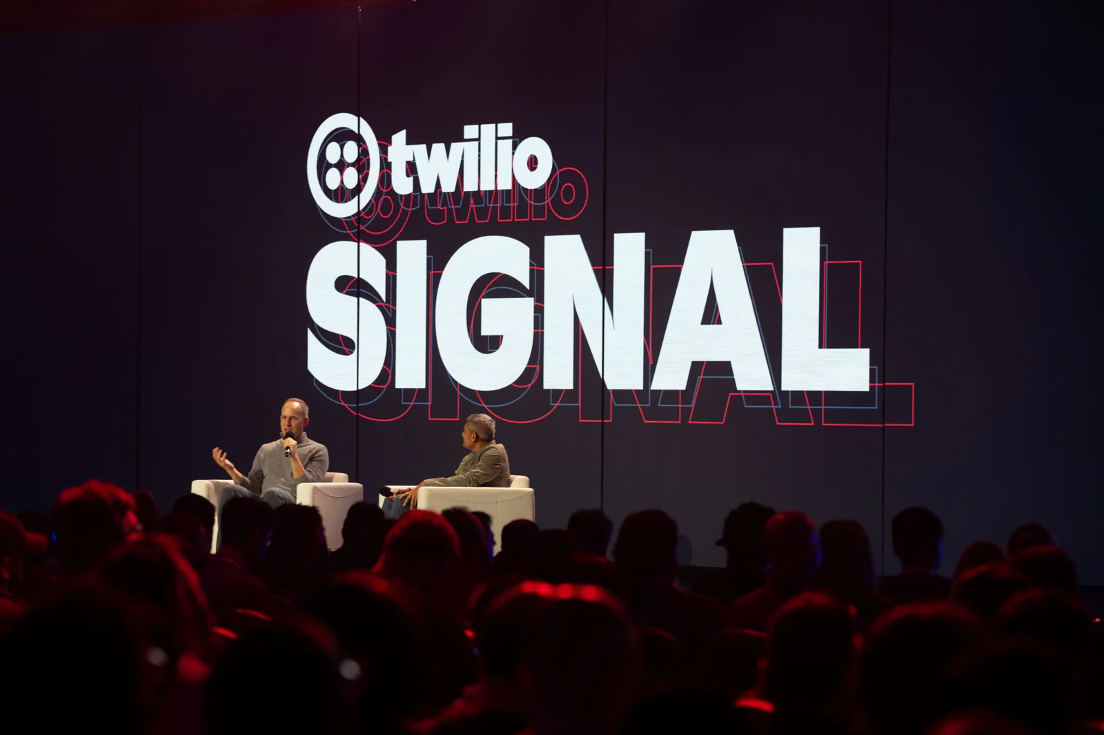 Two people seated on a stage speaking at the Twilio Signal event with a large audience in attendance.