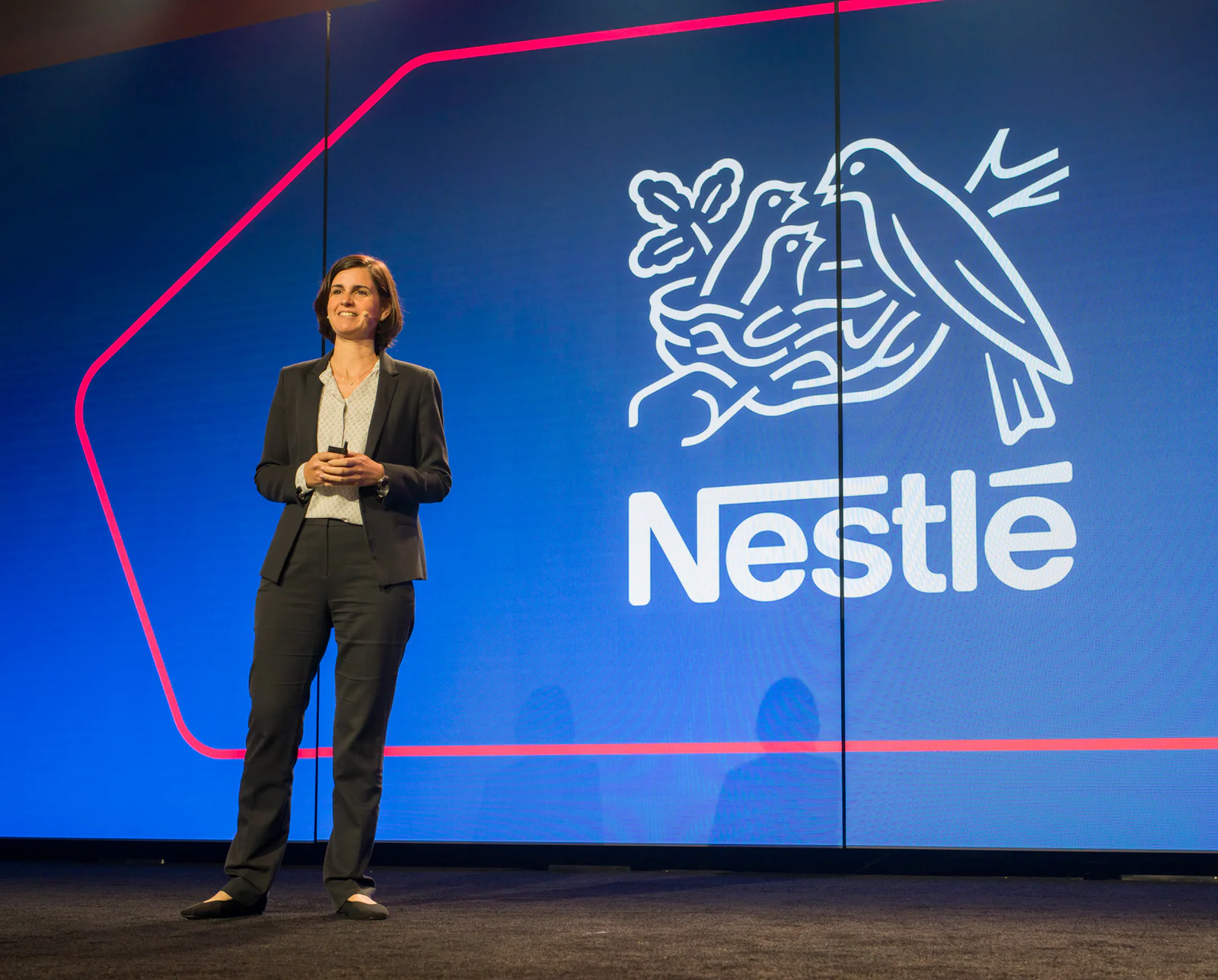 Woman speaking on stage with Nestlé logo on screen