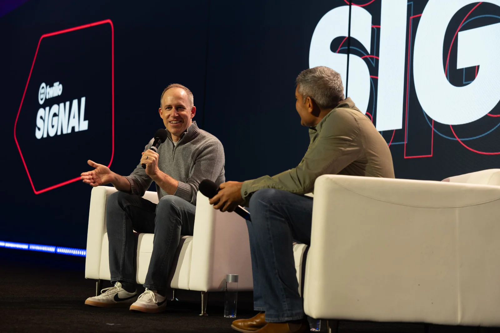 Two men seated on stage, holding microphones, engaged in a discussion at Twilio SIGNAL conference.