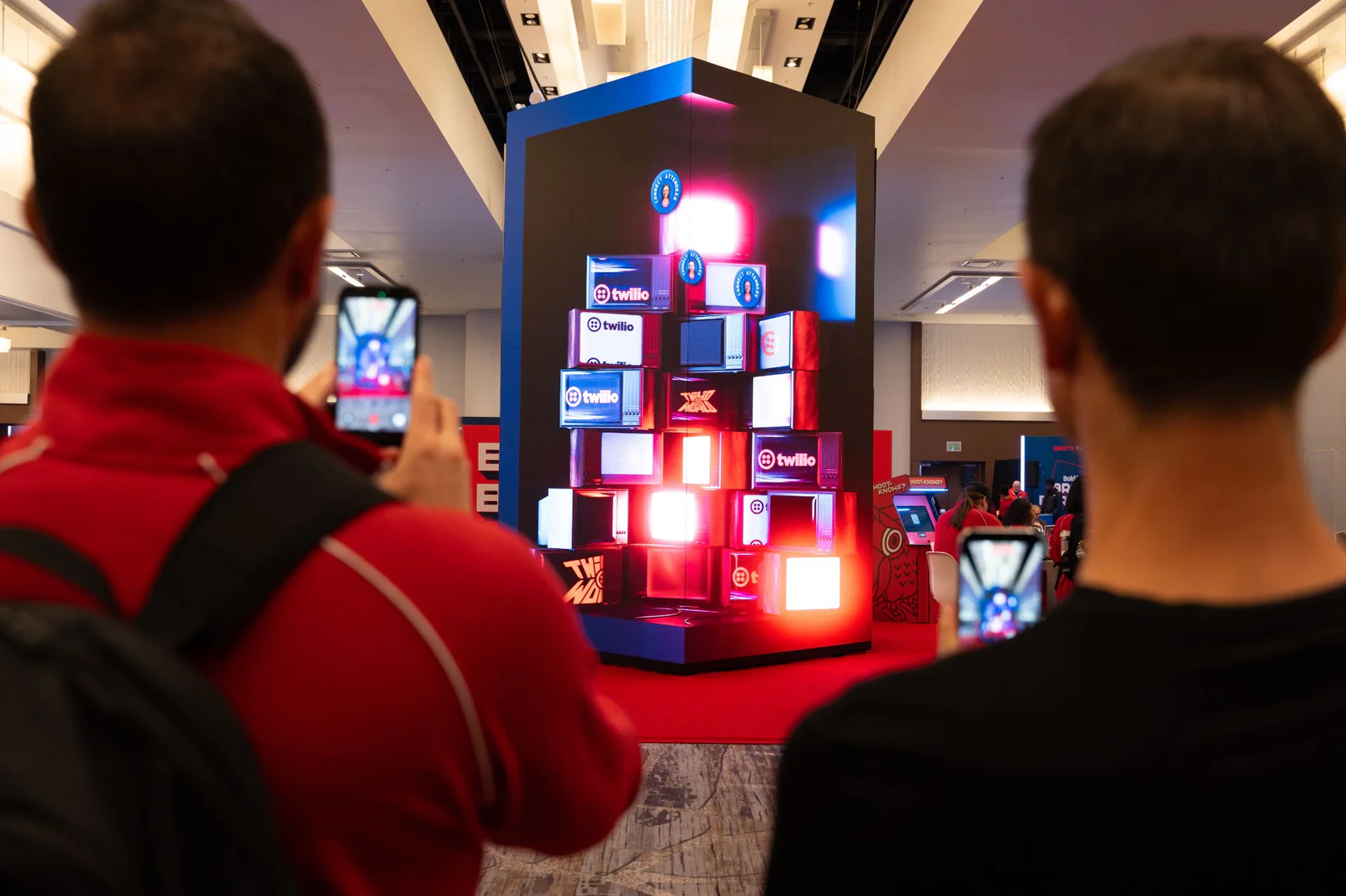Two people taking photos of a digital Twilio display in a conference hall.