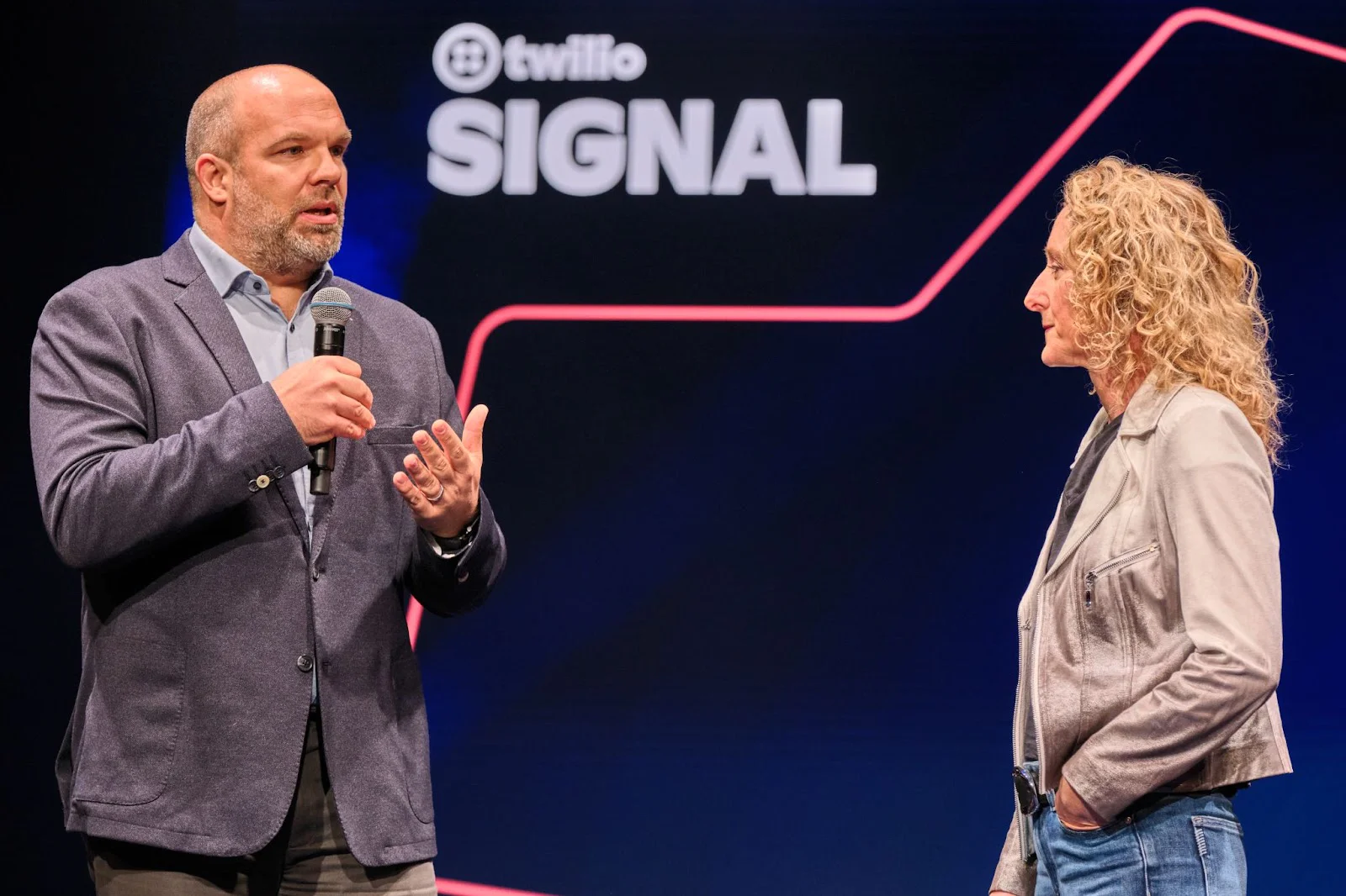 Two speakers on stage at Twilio SIGNAL conference, engaging in a discussion with a microphone.