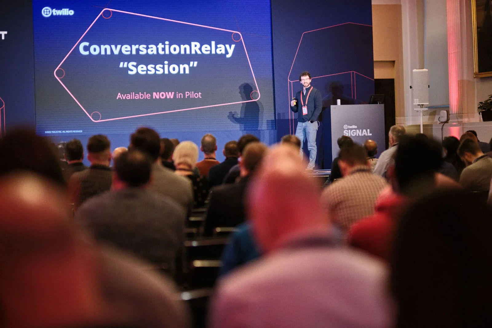 Speaker on stage with a presentation screen at a technology conference with an audience listening.