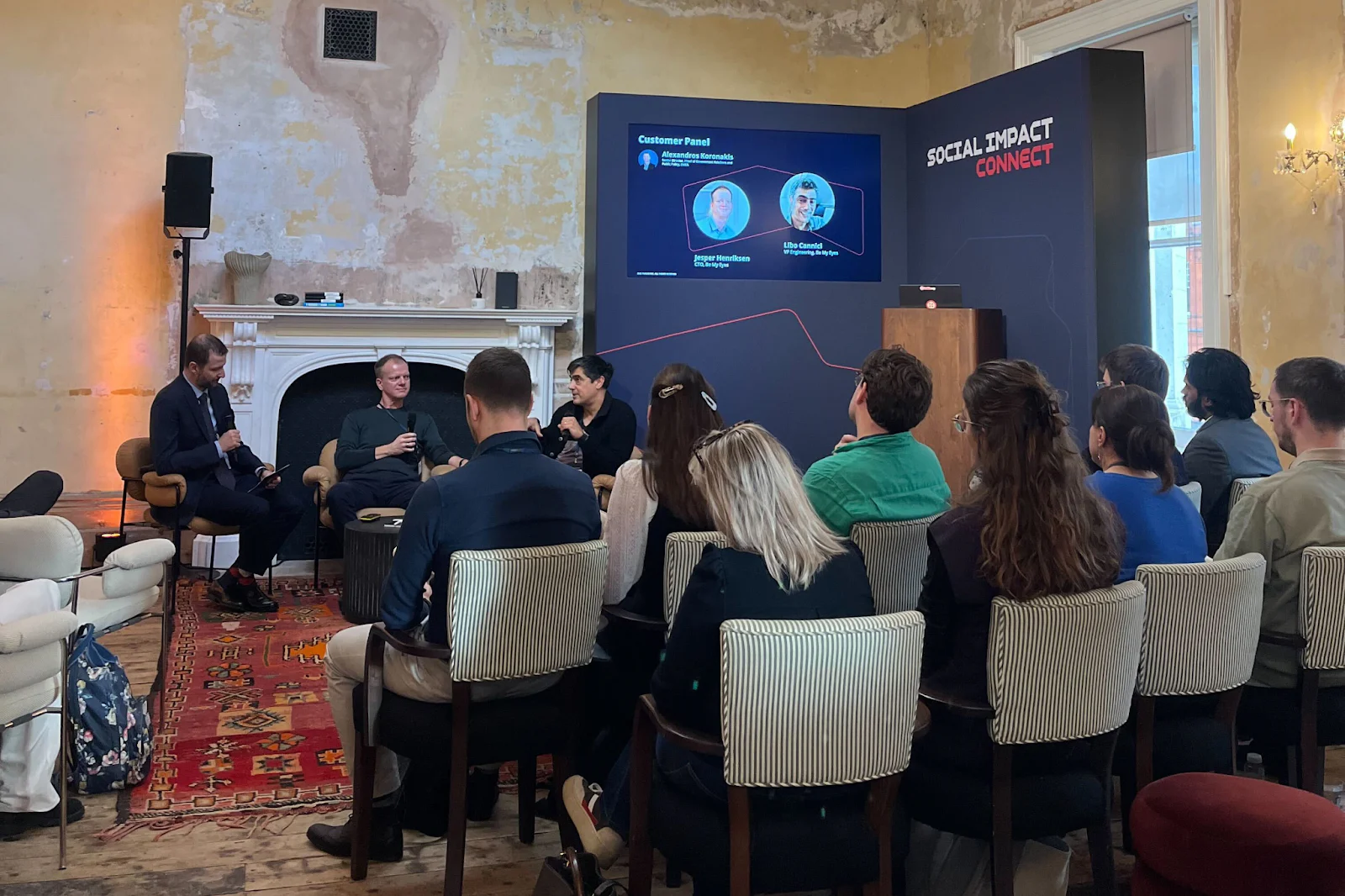 People attending a panel discussion at Social Impact Connect, with a screen displaying speakers' information.