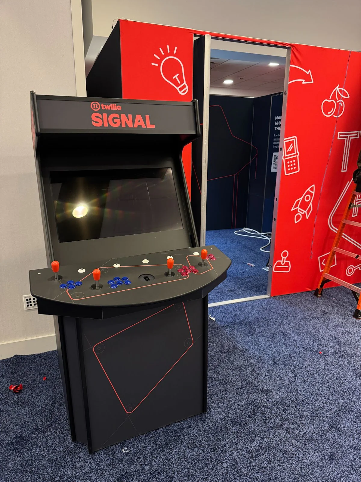 Twilio Signal arcade machine with joystick and buttons stationed by a red booth at a tech conference. Twilio Signal arcade machine with joystick and buttons stationed by a red booth at a tech conference.