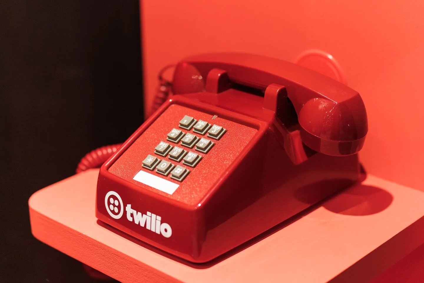 Red rotary phone with Twilio branding on a red shelf. Red rotary phone with Twilio branding on a red shelf.
