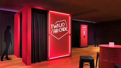 A neon-lit arcade room with Twilio Arcade sign and seating area. A neon-lit arcade room with Twilio Arcade sign and seating area.