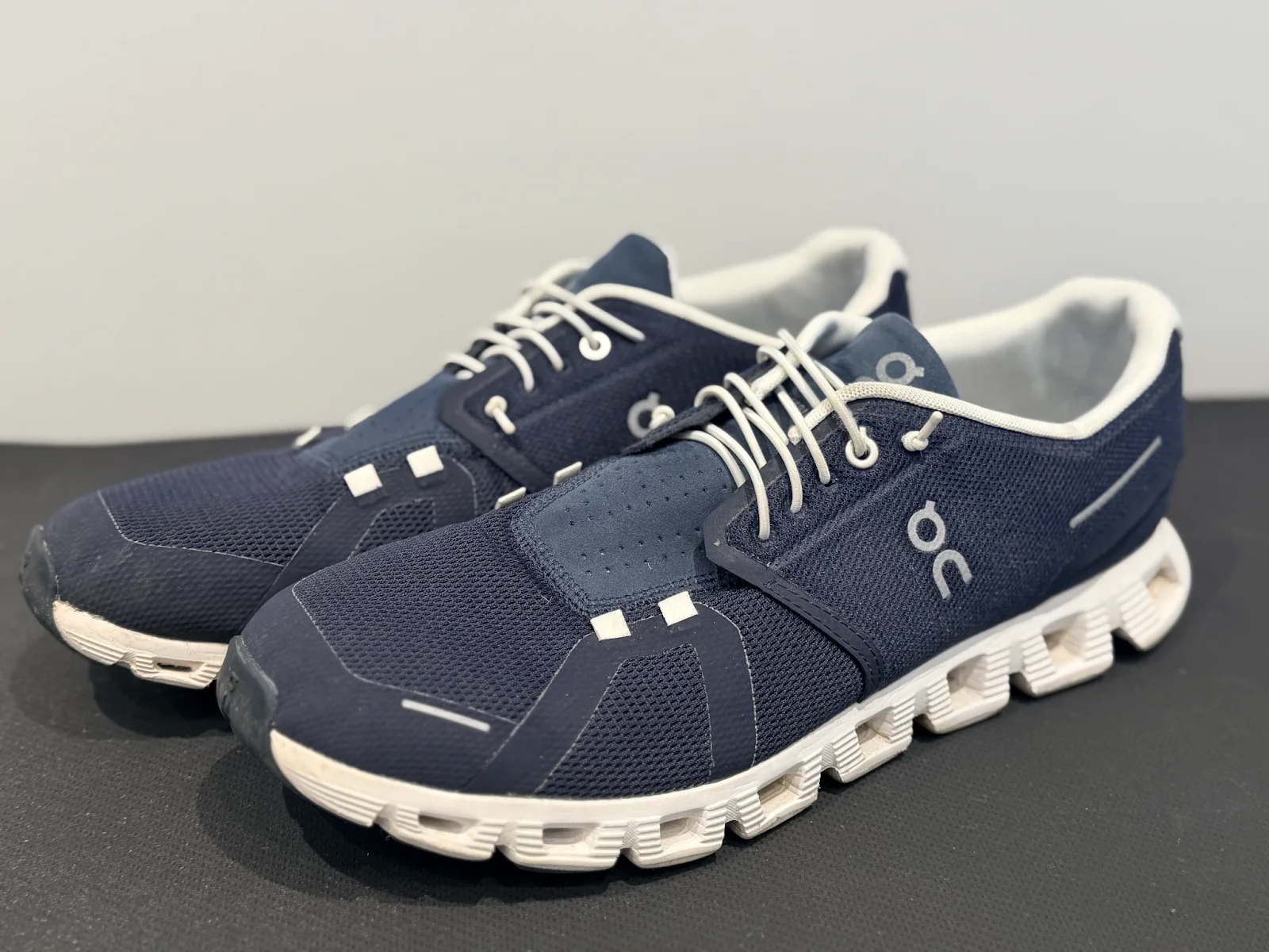 A pair of navy blue sneakers with white laces and white soles.