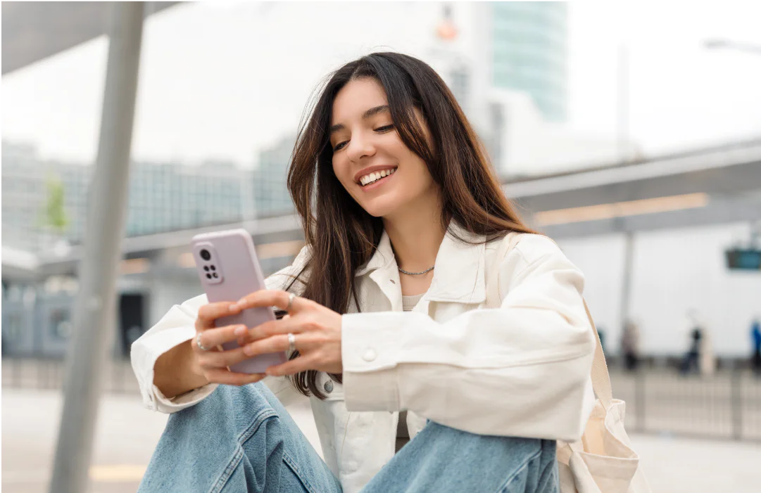 Woman sitting outdoors, smiling, and holding a smartphone